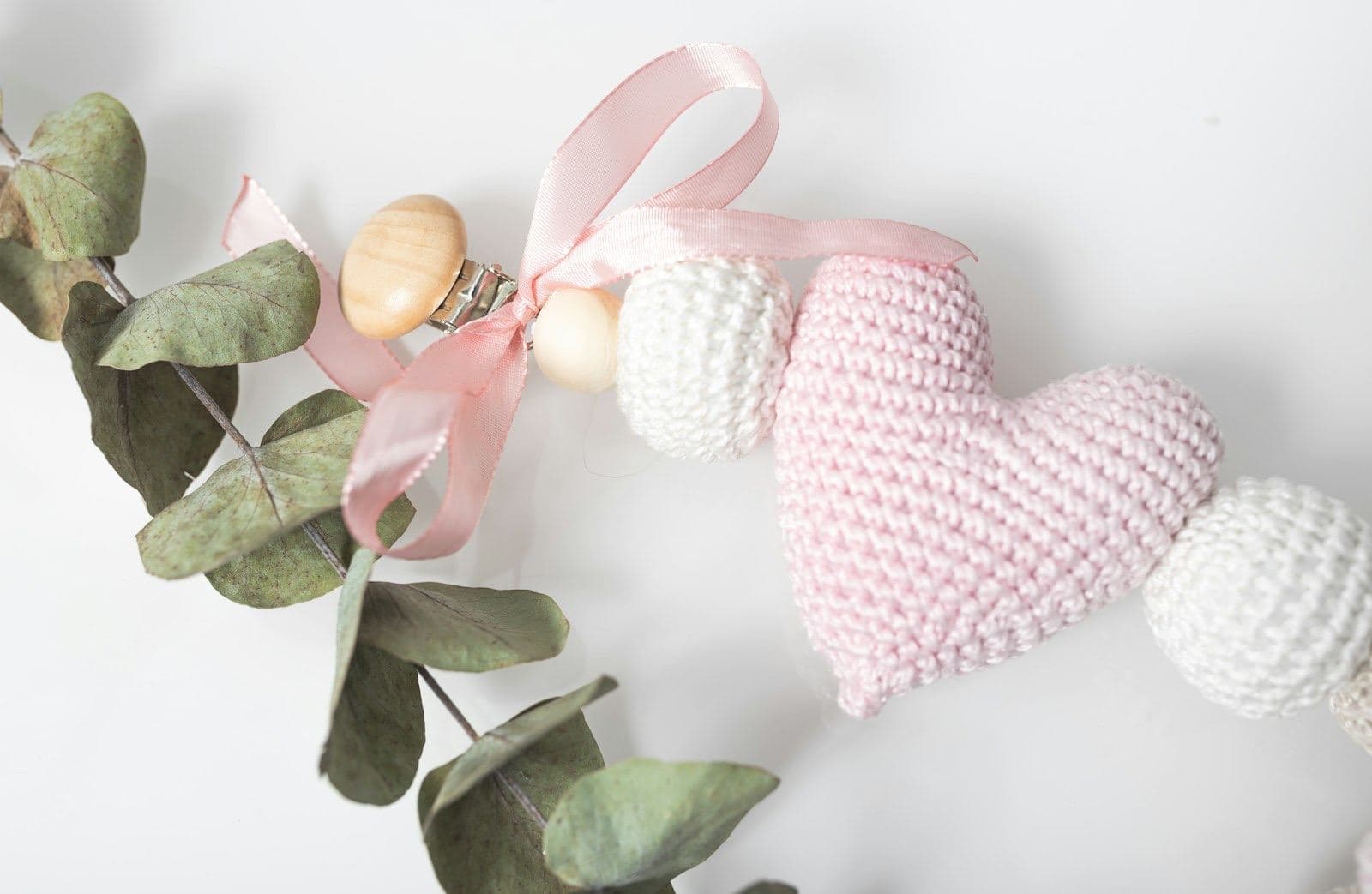 A puffy pale pink crochet heart on a string of white crochet beads with a pink ribbon and eucalyptus (inspiration photo by another maker)